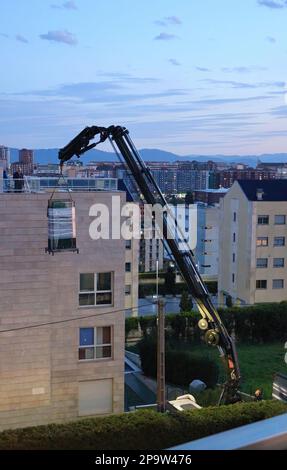 I pannelli di vetro sono consegnati al tetto piano di un blocco di appartamenti da una gru a distanza montata su autocarro al crepuscolo Santander Cantabria Spagna Foto Stock