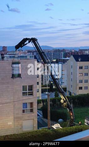 I pannelli di vetro sono consegnati al tetto piano di un blocco di appartamenti da una gru a distanza montata su autocarro al crepuscolo Santander Cantabria Spagna Foto Stock