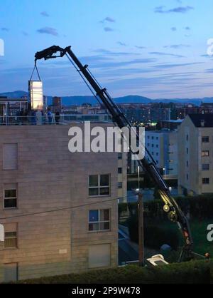 I pannelli di vetro sono consegnati al tetto piano di un blocco di appartamenti da una gru a distanza montata su autocarro al crepuscolo Santander Cantabria Spagna Foto Stock