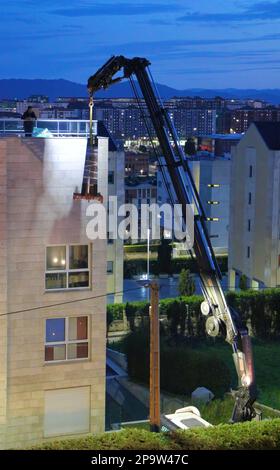 I pannelli di vetro sono consegnati al tetto piano di un blocco di appartamenti da una gru a distanza montata su autocarro al crepuscolo Santander Cantabria Spagna Foto Stock