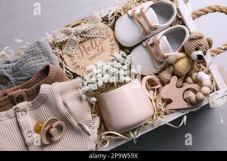 Scatola di legno con abiti per bambini, stivaletti e giocattoli su sfondo grigio, vista dall'alto Foto Stock