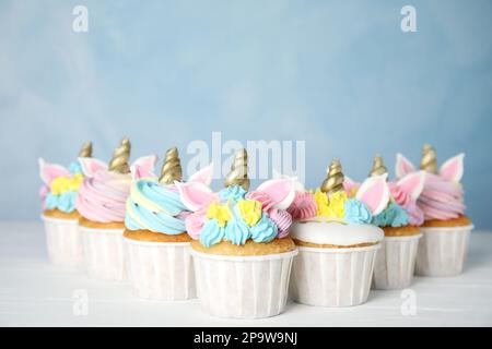 Molti dolci cupcakes unicorno carino su tavolo di legno bianco contro sfondo azzurro Foto Stock