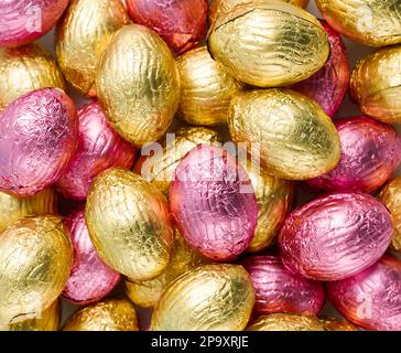 Primo piano di mucchio di uova di caramelle di Pasqua avvolte in foglio rosa e dorato. Buon concetto di Pasqua. Preparazione per le vacanze. Vista dall'alto, macro Foto Stock