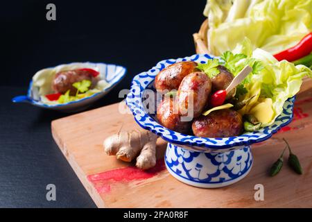 Concetto alimentare Sai krok Isan o Isaan Thai-Laos salsicce fermentate di maiale e riso in tradizionale piatto di ceramica tailandese piedistallo su sfondo nero con copia Foto Stock