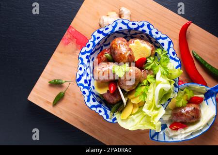 Concetto alimentare Sai krok Isan o Isaan Thai-Laos salsicce fermentate di maiale e riso in tradizionale piatto di ceramica tailandese piedistallo su sfondo nero con copia Foto Stock