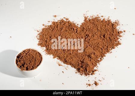 Polvere di cacao a forma di cuore versata, solata su fondo bianco. Foto Stock