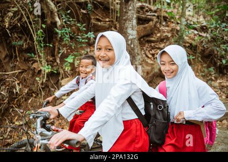 tre studenti delle scuole elementari in bicicletta insieme Foto Stock