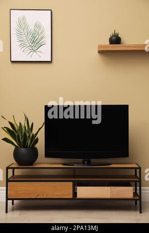TV moderna su armadio e piante verdi vicino alla parete beige in camera. Design degli interni Foto Stock