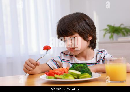 Carino ragazzino che si rifiuta di mangiare verdure a casa Foto Stock