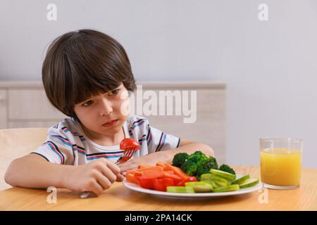 Carino ragazzino che si rifiuta di mangiare verdure a casa Foto Stock