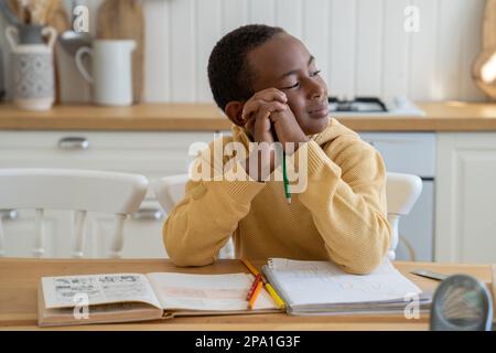 Sorridente bambino sognante ragazzo afroamericano procrastinating sul fare i compiti a casa Foto Stock