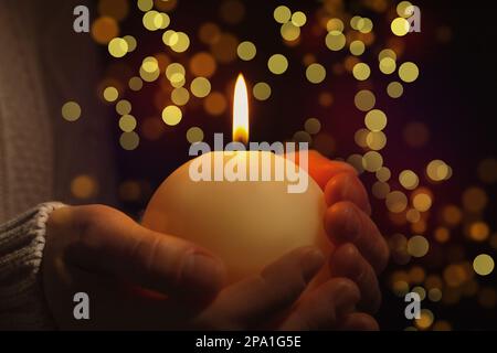 Vista in primo piano della donna che tiene la candela bruciante nel buio, effetto bokeh. Vigilia di Natale Foto Stock