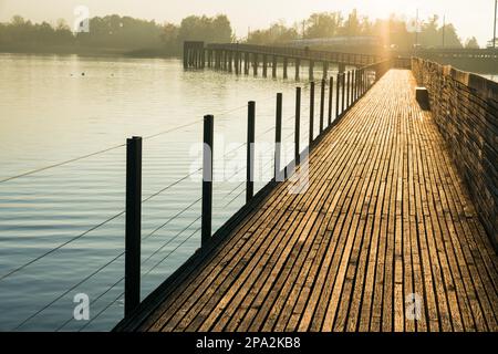 Lungo molo in legno e passerella sul lago di Zurigo vicino a Rapperswil in una luce dorata della sera con una silhouette di montagne sullo sfondo Foto Stock