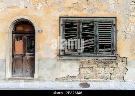 Facciata fatiscente con persiane rotte e una porta rustica in legno marrone nel villaggio di Neunkirch in Svizzera Foto Stock