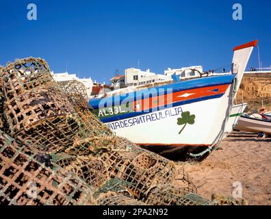 ALBUFEIRA, PORTOGALLO-GENNAIO 05 2019: Colorata barca da pesca in legno sulla spiaggia con cielo blu chiaro. Case per le vacanze sullo sfondo Foto Stock