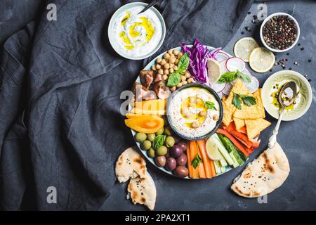 Piatto di meze con hummus, salsa allo yogurt, spuntini assortiti. Spazio per il testo. Hummus, bastoni di verdure, ceci, olive, pita, chip. Piastra, centrale Foto Stock