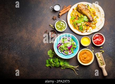 Piatti indiani tradizionali assortiti, vista dall'alto del pollo biryani con riso basmati, pane naan, antipasti diversi, salse e chutney, in stile rustico Foto Stock