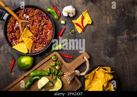 Chili con carne in padella su fondo di legno scuro. Ingredienti per preparare il chili con carne. Spazio per il testo. Vista dall'alto. Peperoncino con carne, nachos Foto Stock