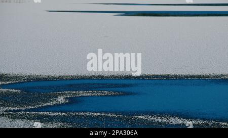 Lago parzialmente ghiacciato con neve distesa sul ghiaccio Foto Stock