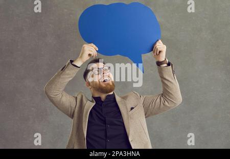Felice giovane uomo che tiene un balloon di discorso che ripartisce i suoi pensieri e le idee di affari Foto Stock
