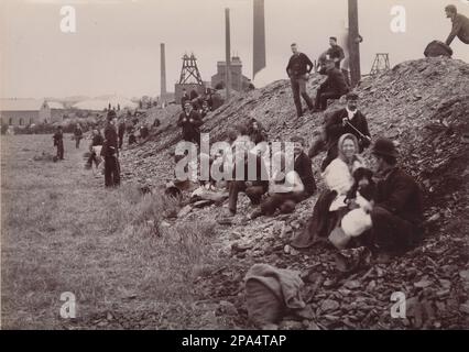 Famiglie che raccolgono carbone da un cumulo di suolo in collisione. La fotografia dei primi anni del 20th ° secolo mostra uomini, donne e bambini che smistano attraverso il materiale di scarto prodotto dalla miniera in cerca di carbone per portare a casa per il carburante. Gli edifici di Colliery possono essere visti sullo sfondo, compreso un camino e una ruota di pozzo. Un poliziotto sta guardando i raccoglitori. È probabile che la fotografia sia stata scattata durante uno degli scioperi dei minatori del 20th° secolo Foto Stock