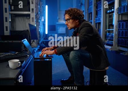 Tecnico IT che utilizza un computer portatile mentre lavora nel data center Foto Stock