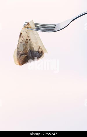 Borsa da tè triangolare usata appesa a una forchetta contro uno sfondo bianco. Il sacchetto del tè è punte di PG biodegradabili della pianta non ha basato la plastica. Foto Stock
