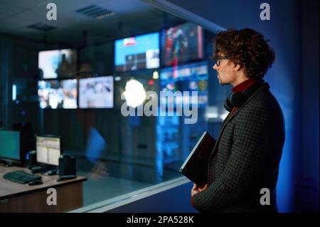 Uomo che guarda la riflessione dello schermo del computer nella finestra della stanza del server Foto Stock