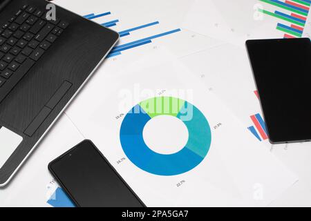 Un ambiente di ufficio moderno con telefono cellulare, tablet, grafico a torta e altri materiali di consumo sulla scrivania bianca Foto Stock