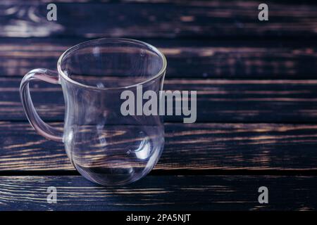 Tazza di vetro vuota sul tavolo di legno scuro e sfondo nero bello Foto Stock