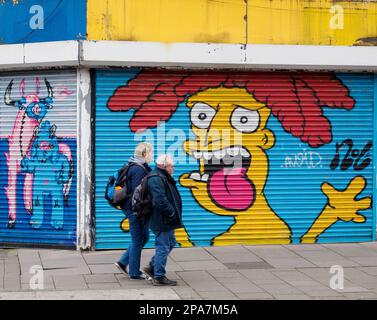 Un uomo e una donna che passano tranquillamente sorprendenti graffiti sulle persiane di un negozio a Bristol UK Foto Stock