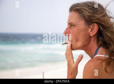 donna che fuma un giunto sulla spiaggia Foto Stock