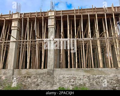 Un edificio incompiuto con pilastri in cemento e pali di bambù come sostegni. Foto Stock