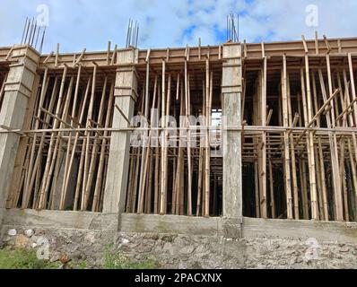 Un edificio incompiuto con pilastri in cemento e pali di bambù come sostegni. Foto Stock