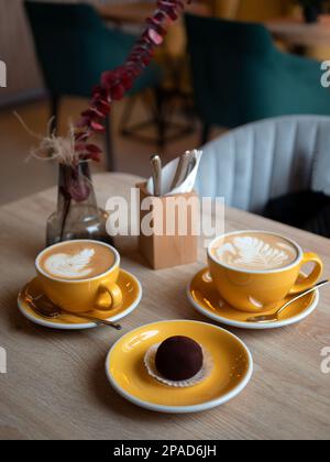 Tazze di caffè giallo brillante con caffè e torta al cioccolato sul tavolo, primo piano. Dessert nella caffetteria, focus selettivo Foto Stock