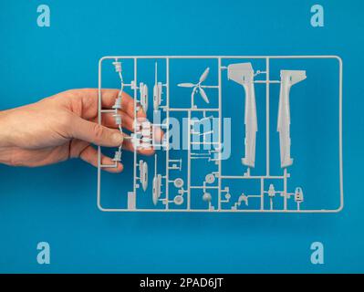 Canale di colata da un kit modello in plastica in mano su sfondo blu. Albero delle parti del modello di aeroplano, primo piano. Costruzione di aerei modello, concetto di hobby Foto Stock