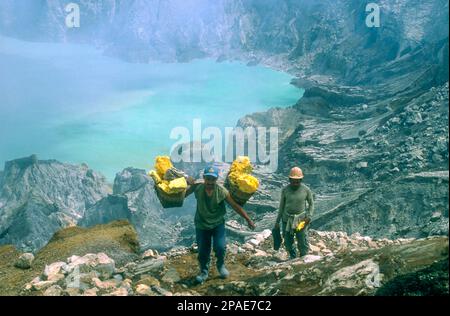 I lavoratori della miniera di zolfo si trudono in salita dal cratere di Kawah Ijen a Giava Orientale, Indonesia Foto Stock