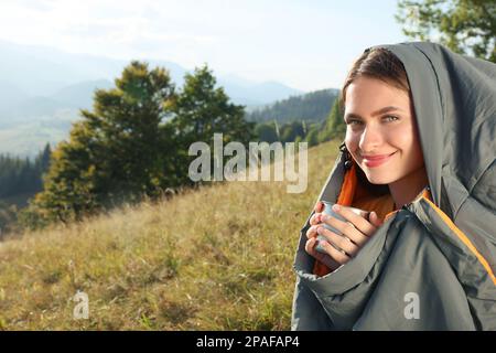Giovane donna con drink in sacco a pelo circondato da una bella natura Foto Stock