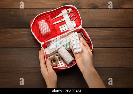 Donna che prende pillole da kit di primo soccorso a tavolo di legno, vista dall'alto Foto Stock