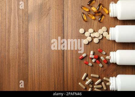 Bottiglie rovesciate con supplementi dietetici diversi su tavolo di legno, piatto. Spazio per il testo Foto Stock
