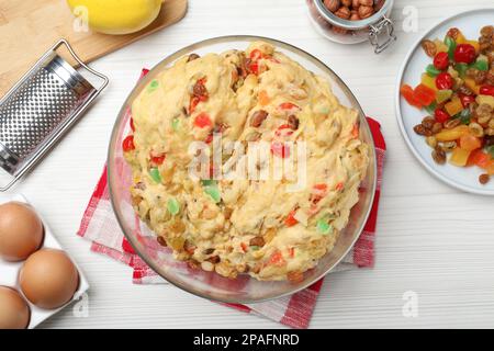 Pasta cruda con canditi e noci per Stollen circondata da ingredienti su tavola di legno bianco, piatto. Cottura tradizionale tedesco brea di Natale Foto Stock