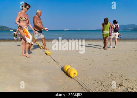 Una coppia turistica a Patong Beach, Phuket, Thailandia, passando su una linea di boe che delimitano le aree per il nuoto e per gli sport acquatici motorizzati Foto Stock
