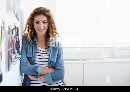 Dopo una carriera nel design grafico. Una giovane grafica sorridente alla fotocamera mentre si trova accanto a una disposizione di foto su una parete. Foto Stock
