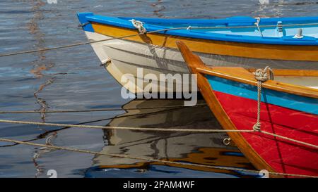 Astratto di due coloratissime clinker costruite barche con riflessi e legate ad un ormeggio con corde. Foto Stock