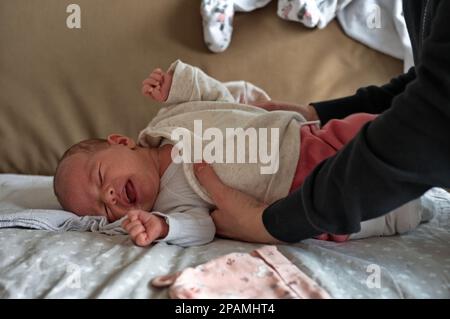 Madre che indossa abiti sulla bambina che piange Foto Stock