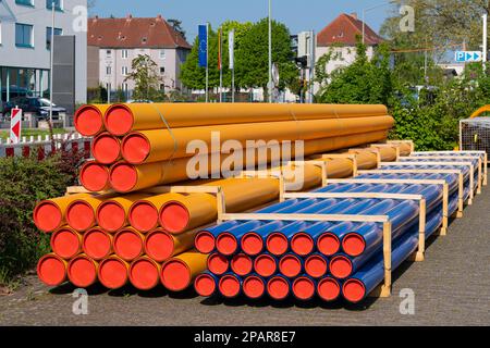 Cantiere in città. Pila di tubi in PVC arancione-giallo e blu. Foto Stock
