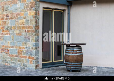 Tavolo da bar a forma di barile di legno davanti ad una porta di vetro. Muro di pietra dell'edificio. Foto Stock