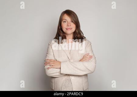 Bella giovane donna incinta sorridente in piedi con le braccia incrociate e guardando la macchina fotografica su sfondo bianco Foto Stock
