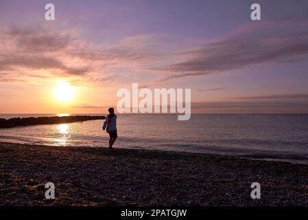 Ragazzo che gioca a lancio di ciottoli sulla spiaggia all'alba. Irriconoscibile, piccola spiaggia di ciottoli, sole, colori giallo e arancione, stile di vita Foto Stock