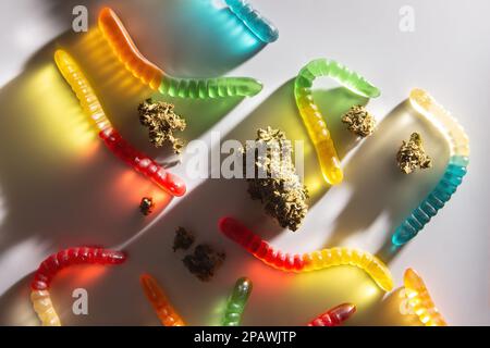 Germogli di marijuana essiccati e vermi di marmellata di colori diversi giacciono su uno sfondo bianco. Vista dall'alto Foto Stock